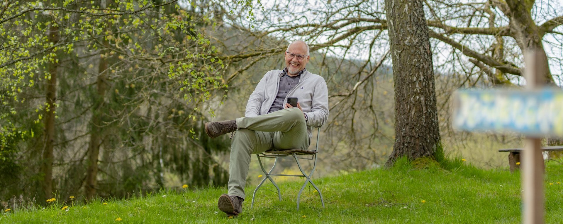 Eine Person sitzt auf einem Stuhl unter einem Baum.